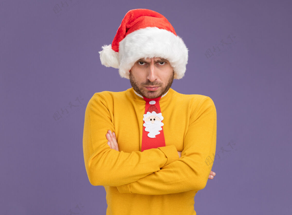 姿势一个戴着圣诞帽打着领带的白人年轻人站在那里 闭着身子 看着隔离在紫色背景上的相机 还有复制空间帽子相机圣诞节