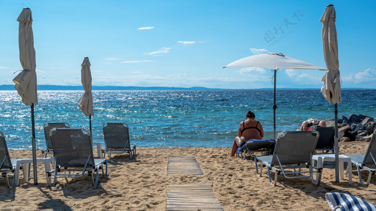 希腊在希腊尼基提 爱琴海海岸的海滩上有雨伞和日光浴床 休息的情侣 靠近水面的岩石风景雨伞海湾