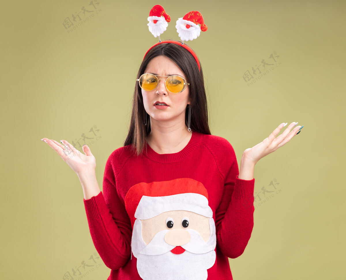 年轻无知的年轻漂亮的白人女孩 穿着圣诞老人的毛衣 戴着眼镜的头带 看着镜头 两手空空的 孤立在橄榄绿的背景上圣诞老人橄榄圣诞老人