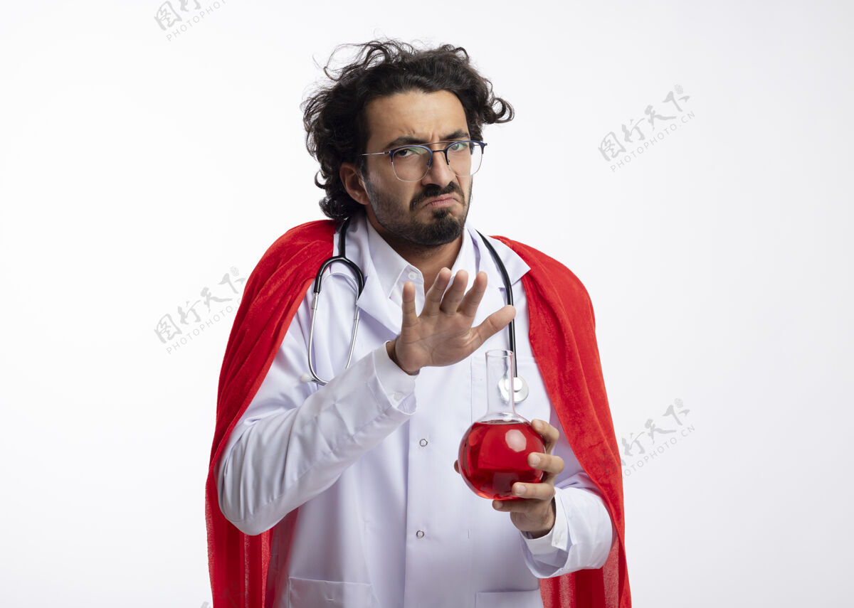 超级英雄一个戴着眼镜 身穿医生制服 披着红色斗篷 脖子上戴着听诊器的年轻白人超级英雄 手里拿着玻璃瓶中的红色化学液体烧瓶医生斗篷