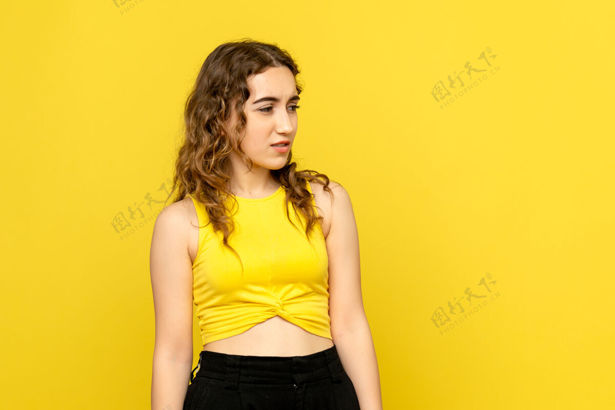 黑发黄色墙壁上表情混乱的年轻女子的正面图前面时尚可爱