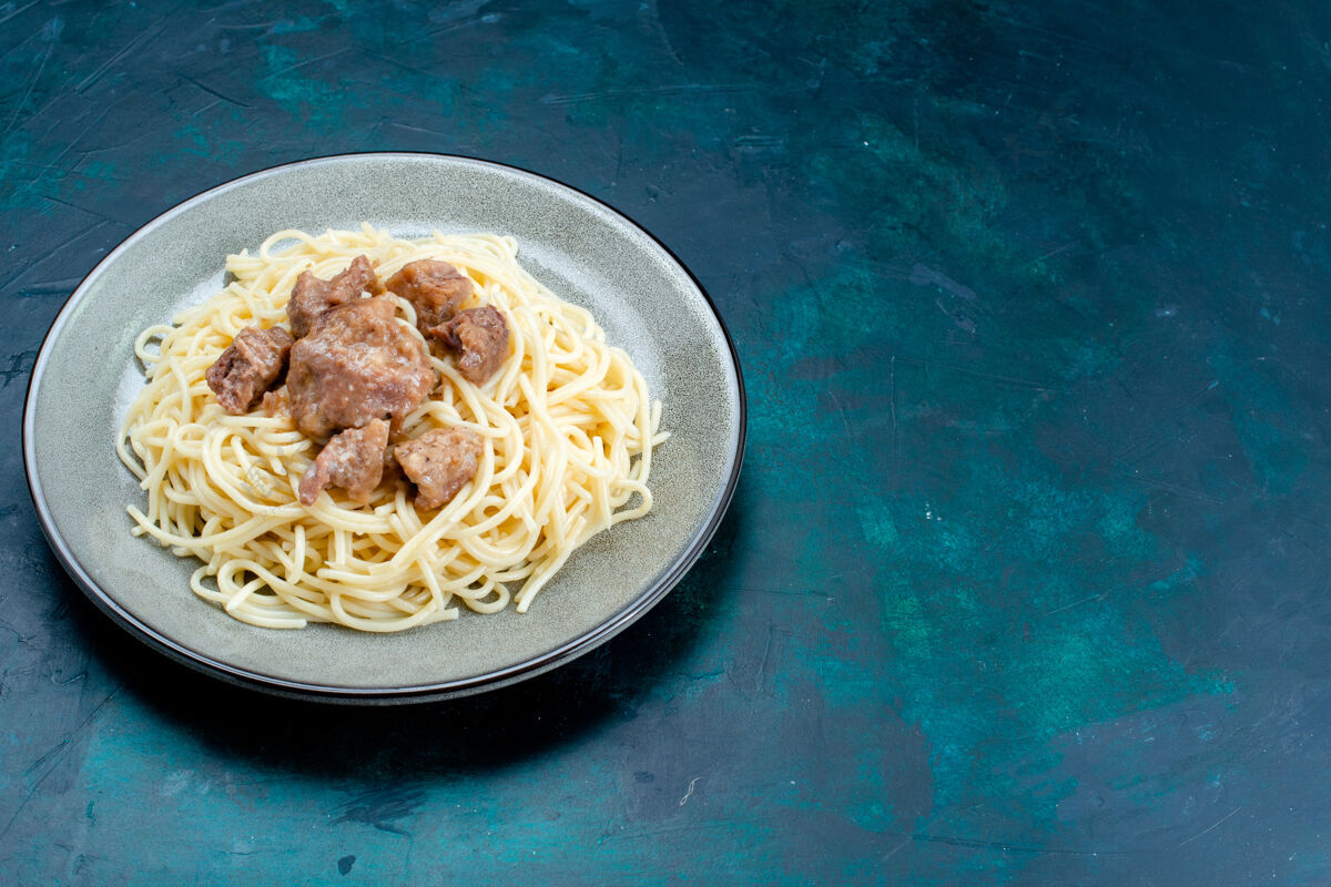 生的半俯视图煮熟的意大利面食 蓝色表面的盘子里有肉片意大利面食意大利餐面团肉肉风景意大利面