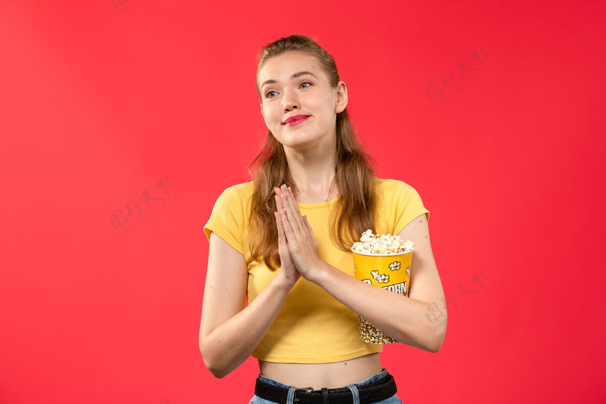 电影正面图年轻女性手持爆米花包 在淡红墙影院摆姿势电影爆米花漂亮