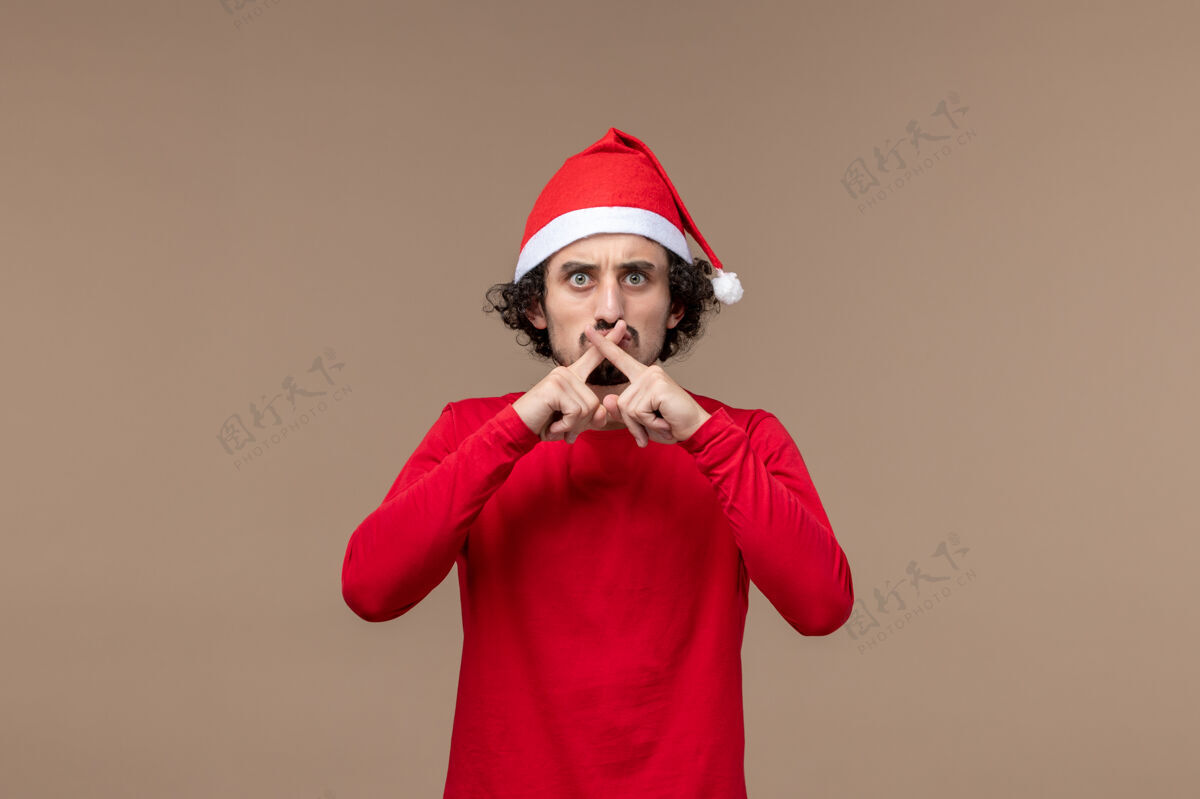 人物正面图：年轻人在棕色背景上交叉手指庆祝圣诞节年轻人交叉节日
