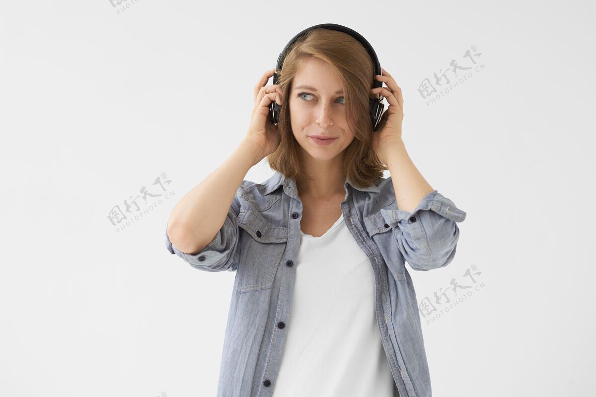 音乐音乐 放松和有趣的概念美丽的现代女孩穿着蓝色衬衫 白色上衣 一边看着一边高兴的表情 通过无线耳机欣赏爵士乐曲目的孤立图片人声音头发
