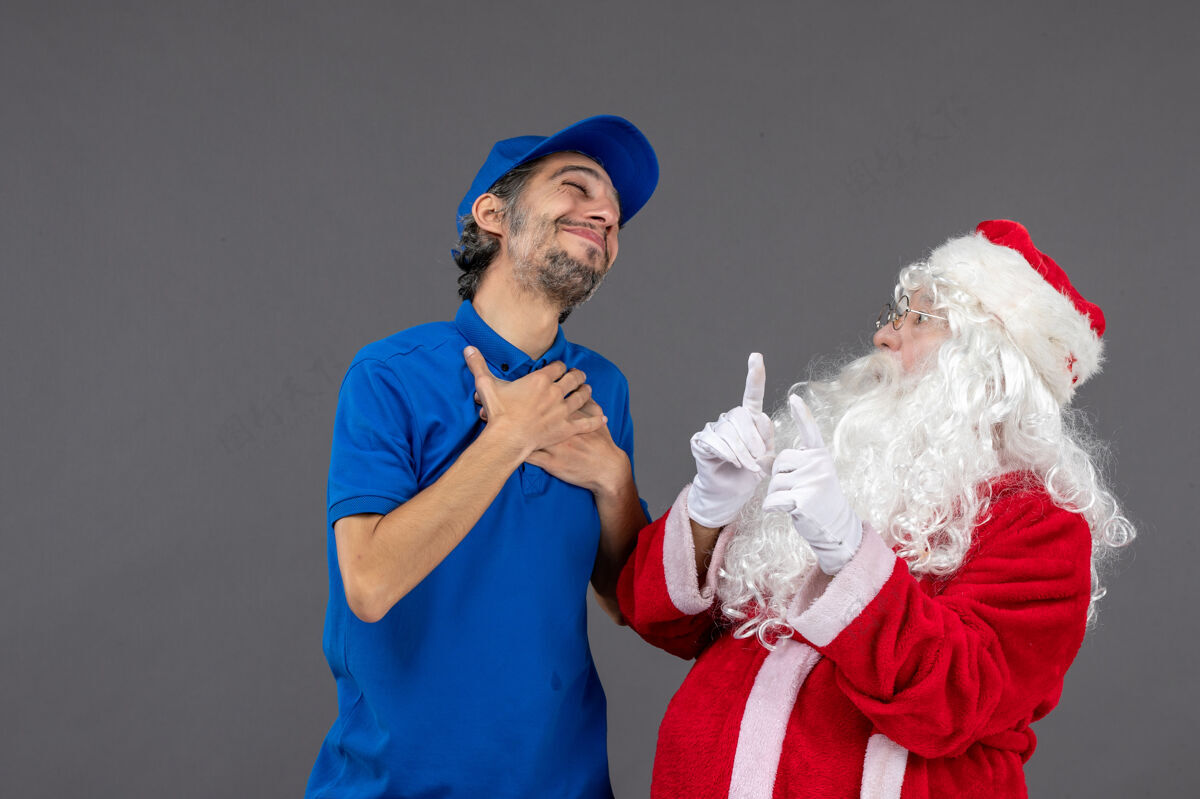 服装灰色墙上的圣诞老人和男信使的正面图圣诞老人圣诞老人情感