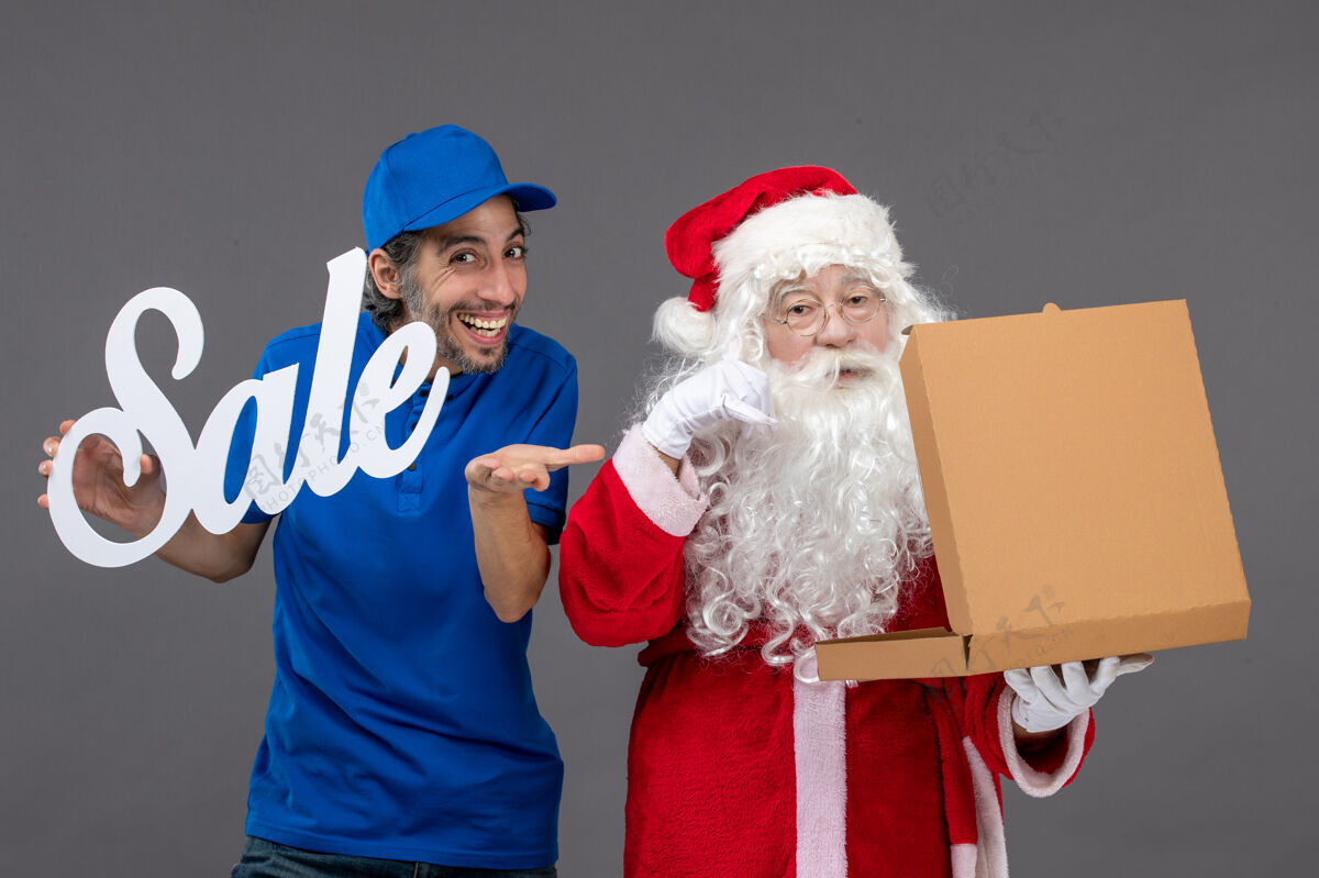 举行圣诞老人的正面图 男信使手持销售横幅 打开灰墙上的食品盒圣诞老人圣诞老人圣诞老人