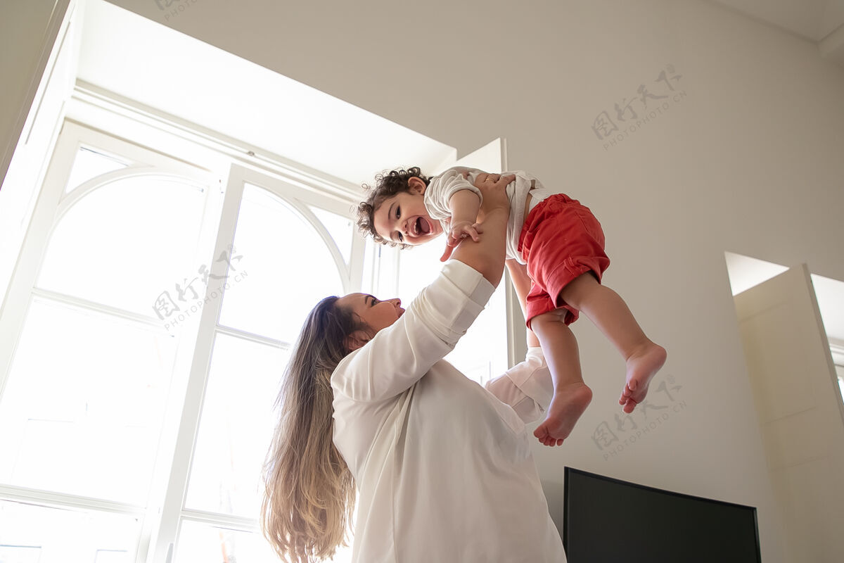 兴奋快乐的妈妈抱着兴奋的宝宝 双手举在空中低角度孩子在家和童年的概念母亲角度可爱
