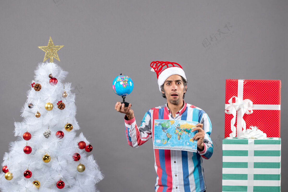 灰色前视图：年轻人举着世界地图和地球仪 举着圣诞树和礼物圣诞快乐假期