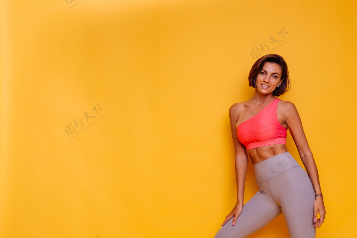 动机年轻健壮的女人穿着运动服 时髦的上衣和紧身裤 对着黄色的墙壁摆姿势成人躯干年轻