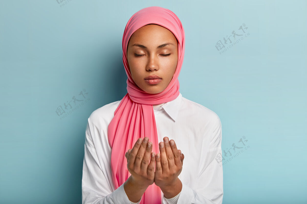 东方阿拉伯忠实的黑皮肤女子双手祈祷 祈求身体健康 信奉健康有面纱的头 穿着白衬衫闭着眼睛享受宁静的气氛祈祷信仰展示