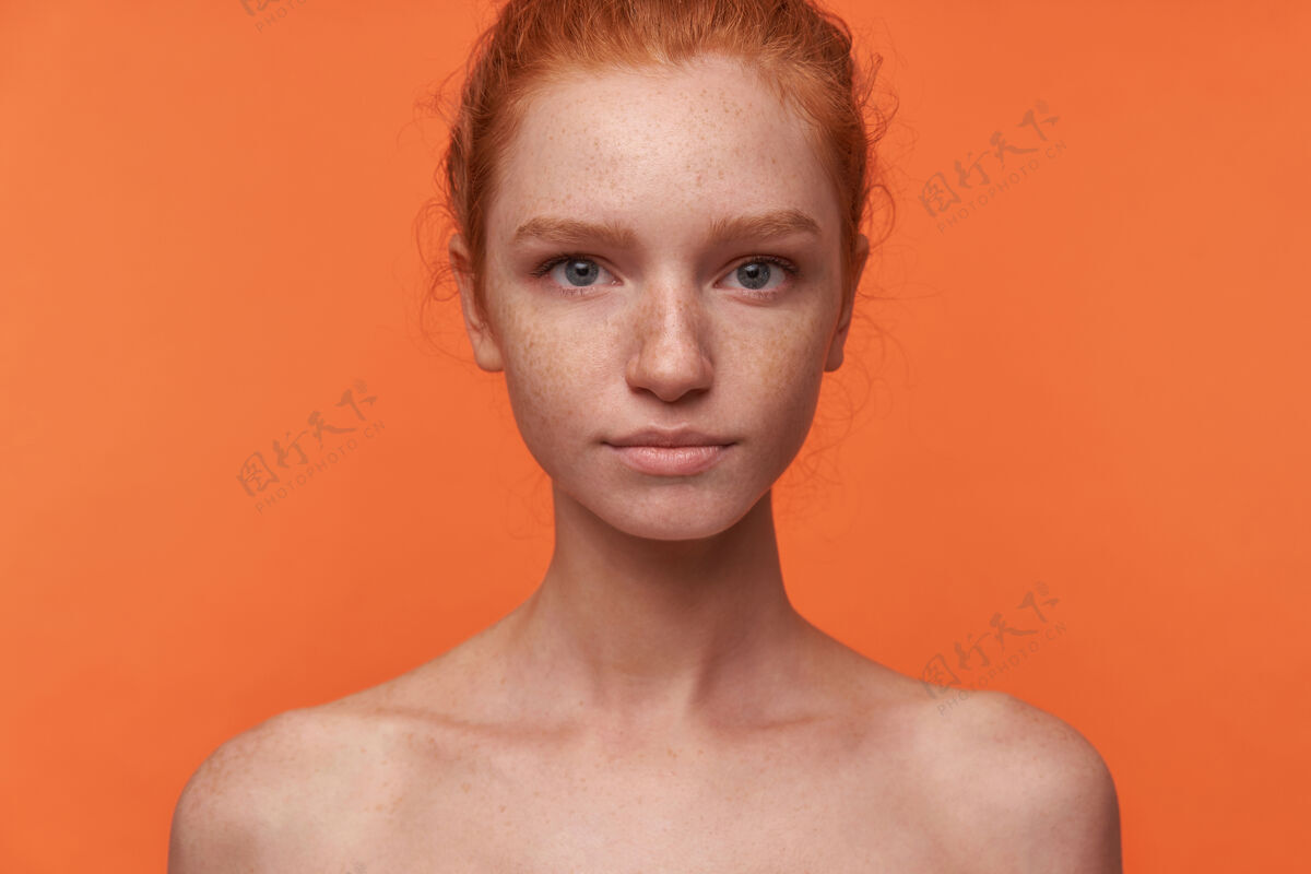 手摄影棚照片：年轻漂亮的readhead女性 随意的发型 站在橙色背景下 不穿衣服 面带平静地看着相机休闲冷静结