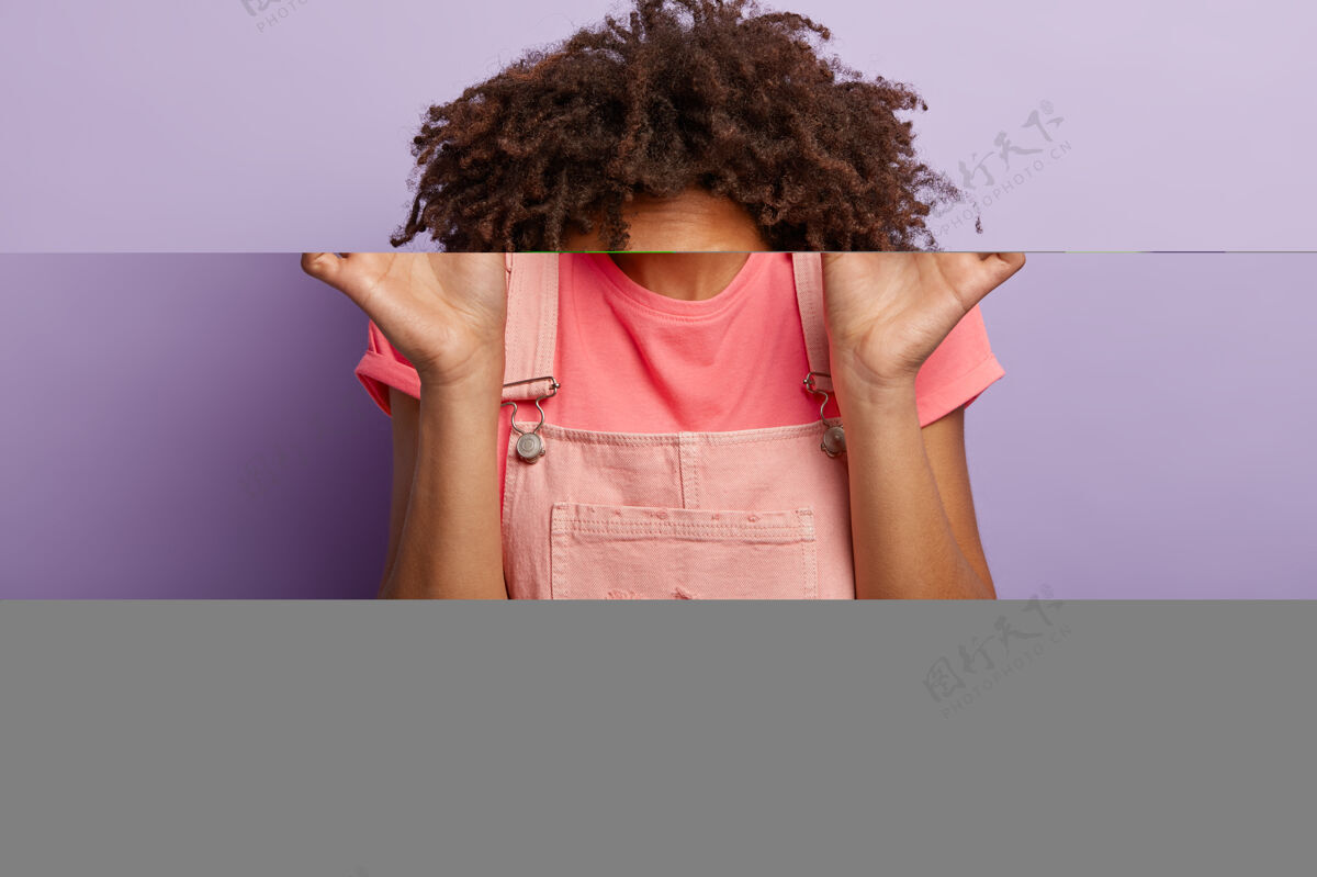 饮食犹豫不决的可爱女人 非洲式发型 包着嘴唇 看着美味的甜甜甜甜圈 含很多热量 穿着休闲装 隔着紫色的工作室墙食物年轻休闲个人