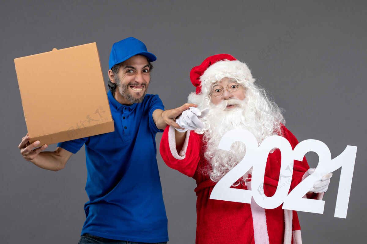 前面圣诞老人的正面图 男信使拿着食物盒 站在灰色的墙上老年人十二月节日