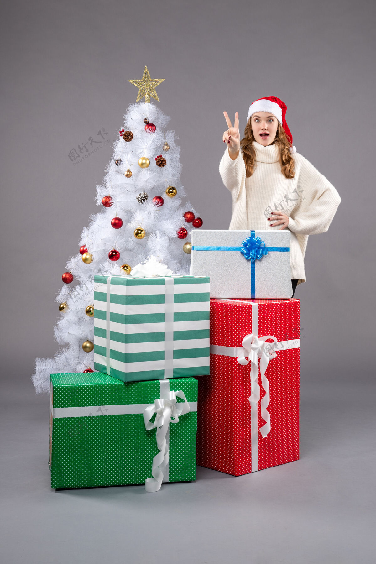 服装年轻的女性在灰色的礼物圣诞树圣诞老人人