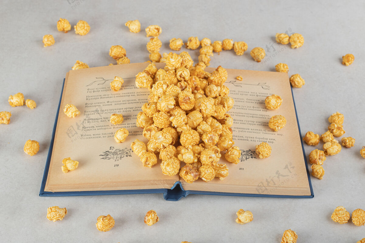 玉米一本打开的书 一堆涂着焦糖的爆米花散落在大理石上书籍零食垃圾