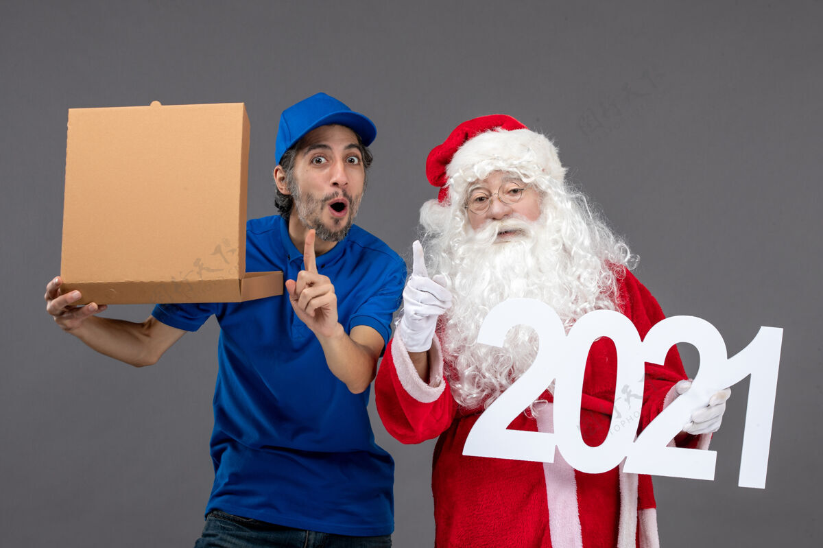 节日圣诞老人的正面图 男信使拿着食物盒 站在灰色的墙上人圣诞快乐圣诞老人