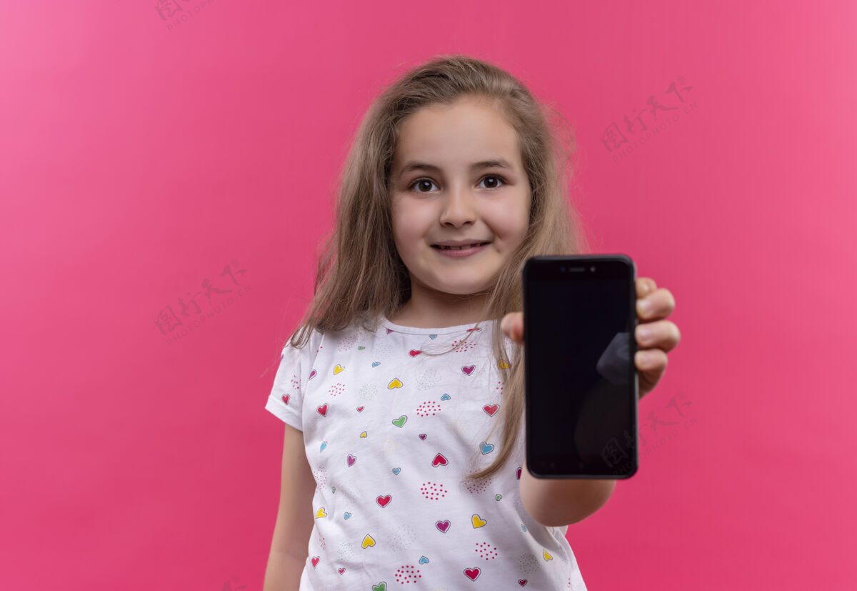 女孩微笑的小女孩穿着白色t恤拿着手机 背景是孤立的粉色白色电话穿着