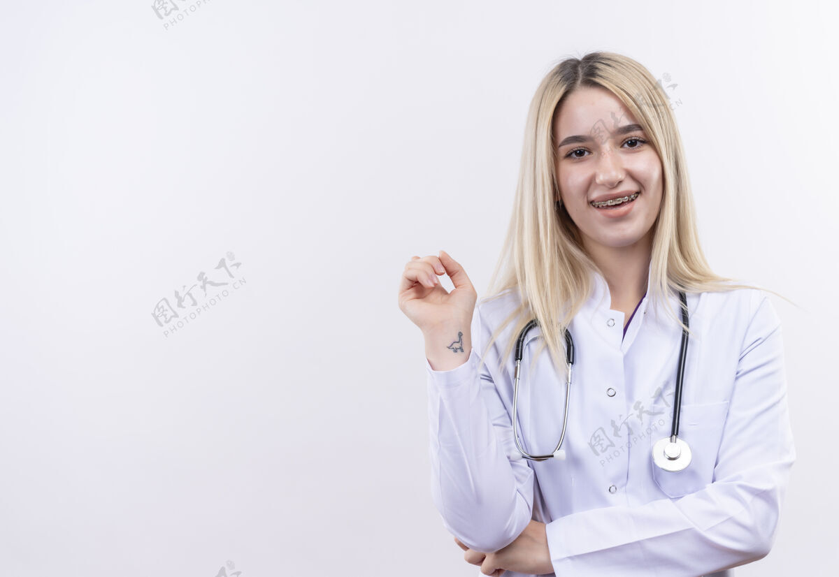 医疗微笑的医生年轻的金发女孩戴着听诊器和医用长袍戴着牙套在孤立的白色背景医生牙科听诊器