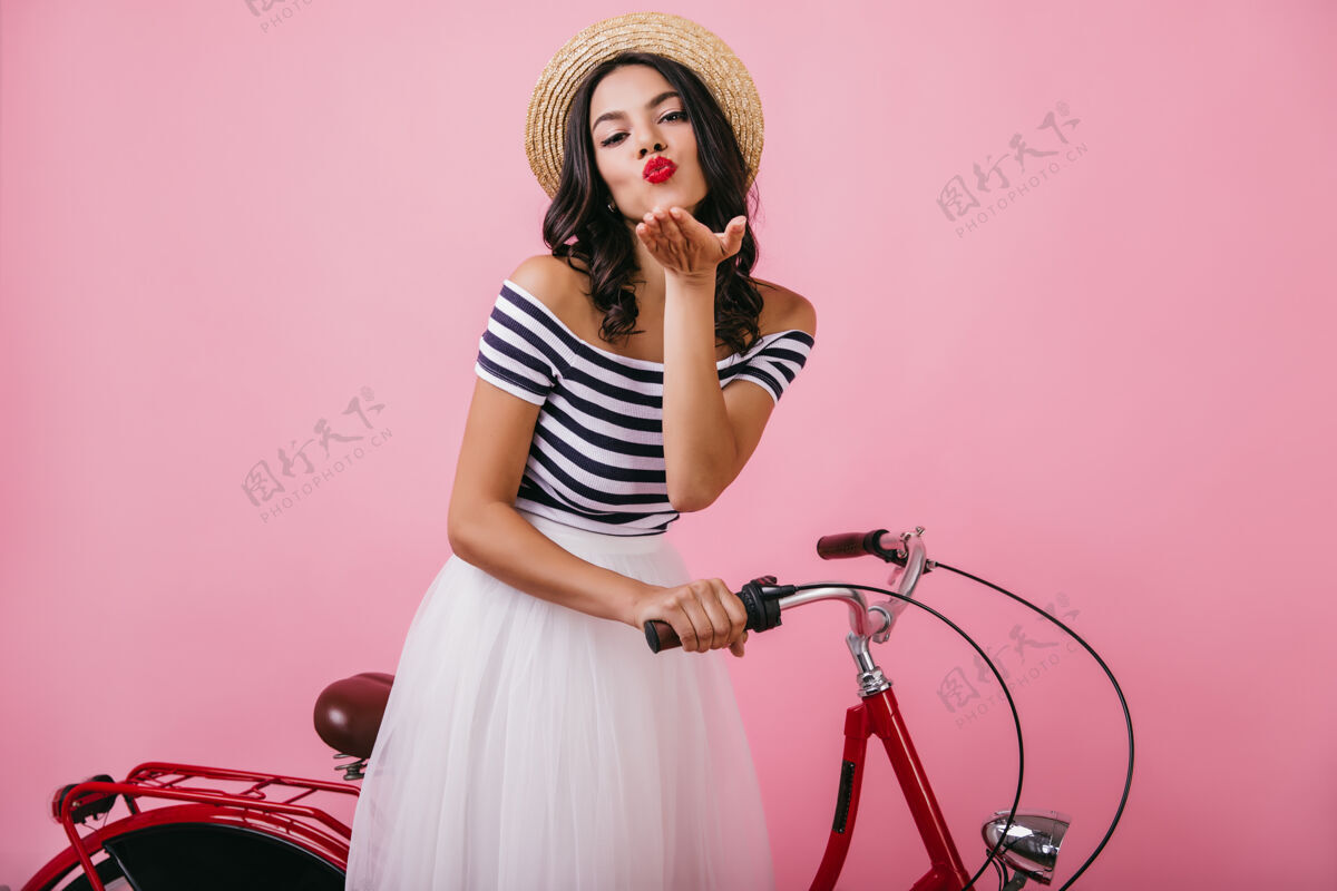 优雅无忧无虑的拉丁女人 优雅的发型 送上空气之吻室内照片 可爱的晒黑女孩在红色自行车旁摆姿势时尚女性浪漫