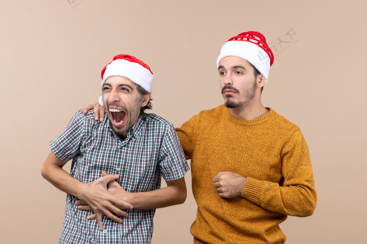 米色正面图两个戴圣诞帽的家伙悲伤的一个把手放在其他人的肩膀上米色的孤立背景圣诞老人前面帽子