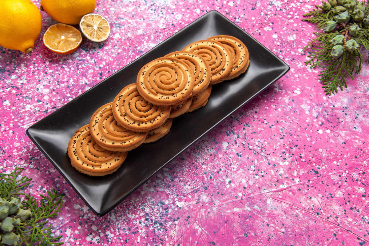 柠檬半顶视图甜饼干美味的小饼干内黑形式与柠檬在淡粉色的桌子上粉色饼干食物