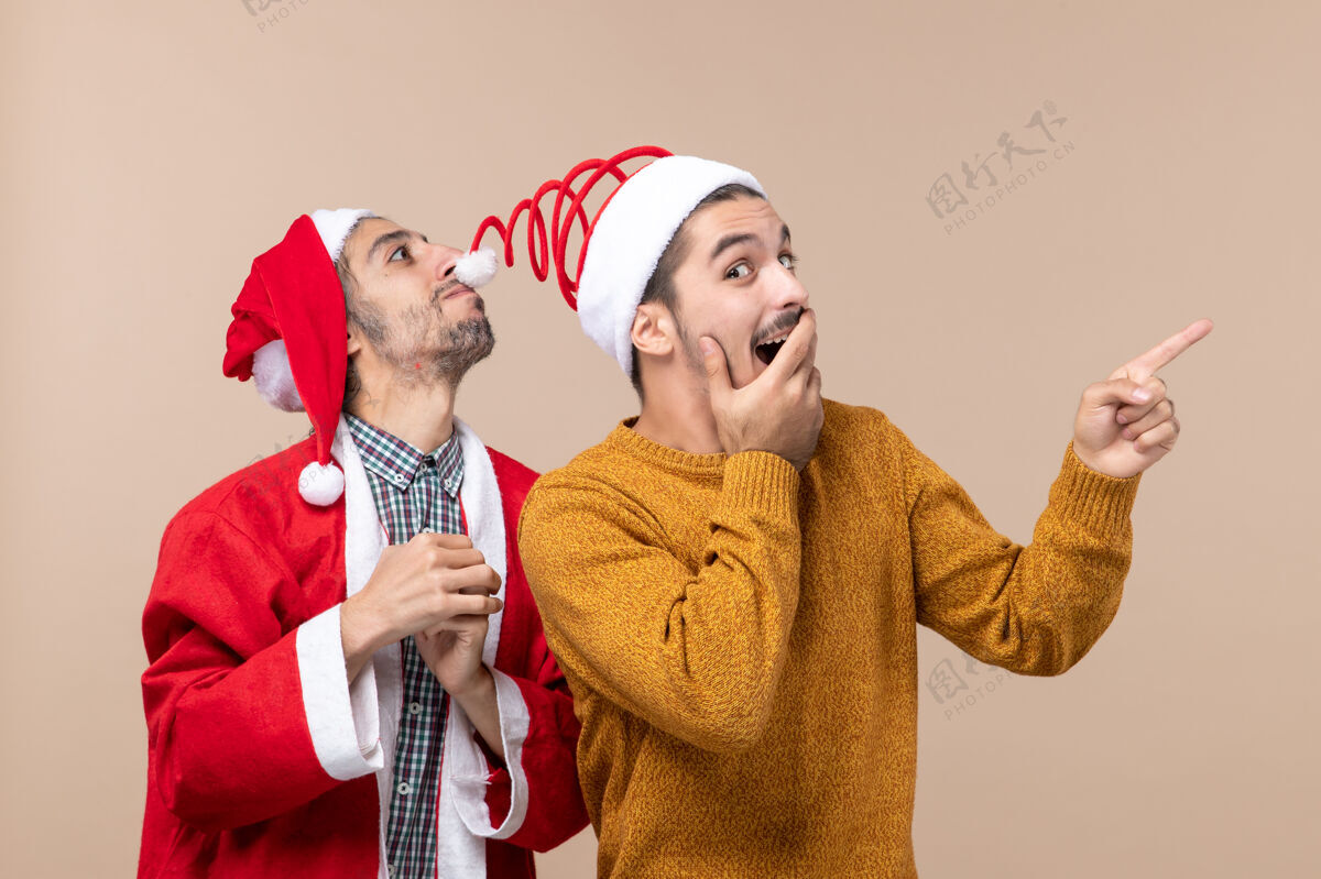 圣诞老人正面图两个戴着圣诞帽的朋友一个戴着帽子 另一个在米色背景上显示方向两个朋友朋友男人
