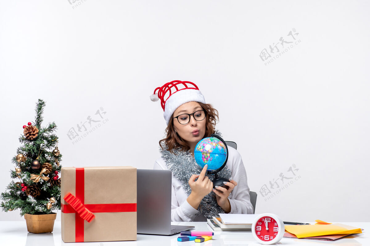 微笑正面图：年轻的女工坐在她的位置前 拿着白色背景上的地球仪视图坐着地球仪
