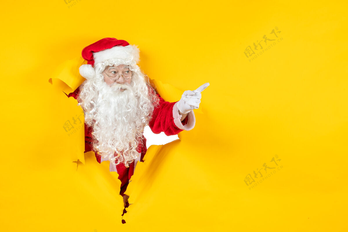 圣诞老人圣诞老人透过撕破的纸黄色墙壁看的正视图圣诞老人圣诞快乐人们