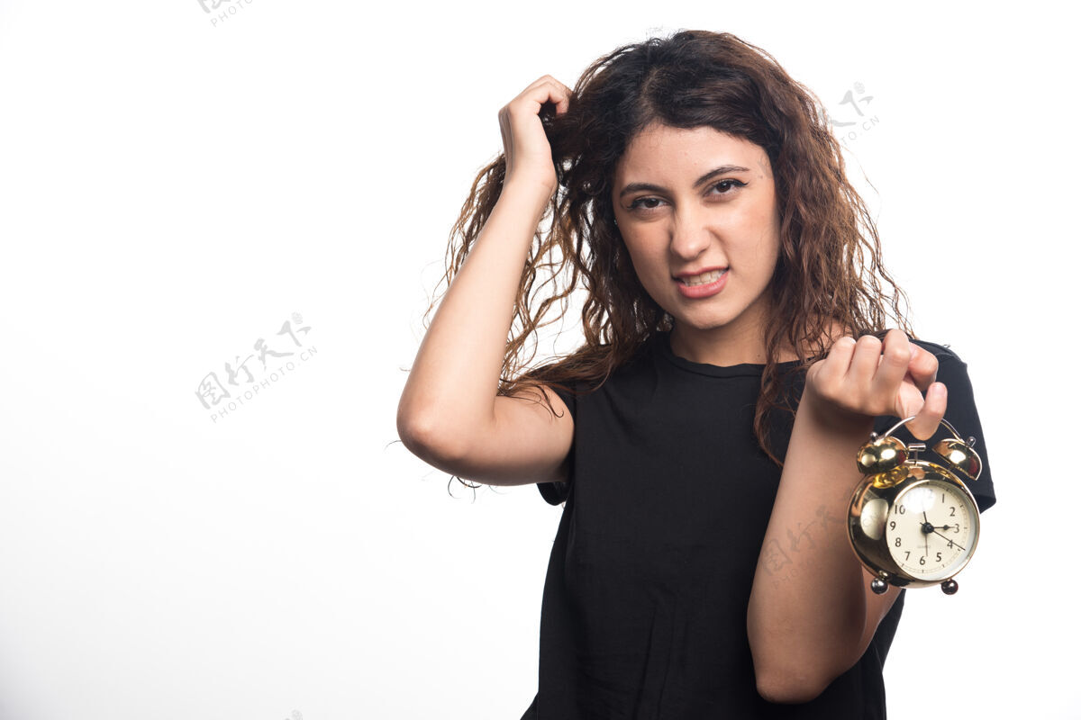 黑发愤怒的女人拿着她的头发和白色背景上的时钟高品质的照片看年轻正式
