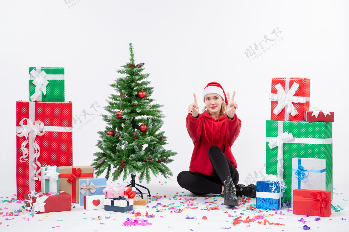 快乐年轻女子坐在白色墙壁上数着节日礼物的前视图冬天计数装饰