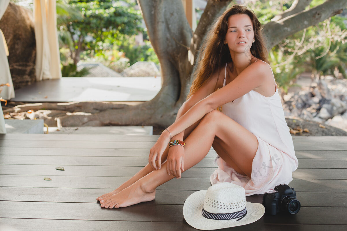 肖像年轻女子光着脚坐在地板上 穿着苍白的连衣裙 微笑着 自然美丽 草帽 数码相机 女人摄影师放松