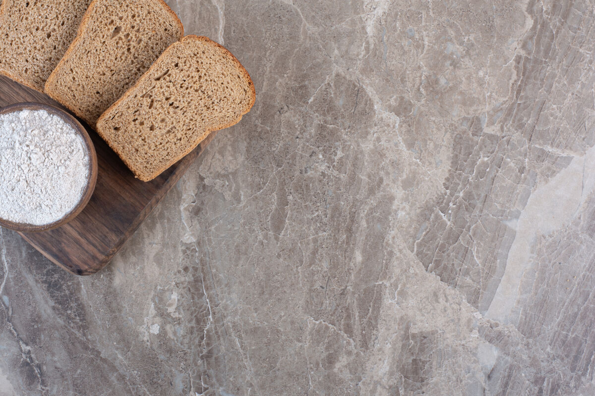 烘焙食品黑面包片和一碗面粉放在大理石板上烘焙商品板