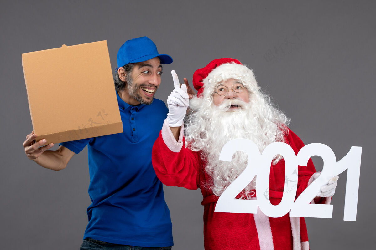 人圣诞老人的正面图 男信使拿着食物盒 站在灰色的墙上人前面帽子