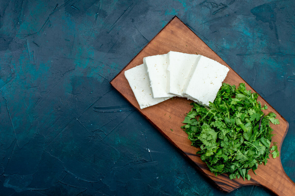 夏天深蓝色表面上白色奶酪和新鲜绿色的顶视图蔬菜生的新鲜