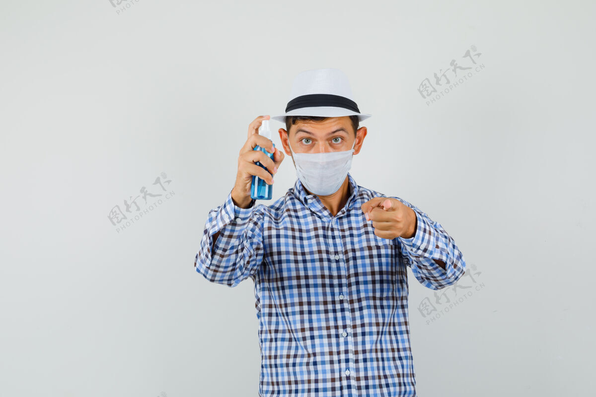 帽子年轻人拿着消毒喷雾 指着穿着格子衬衫的摄像机年轻男性纸