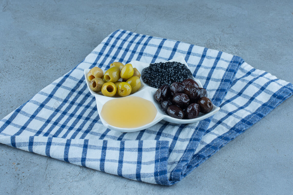 什锦折叠桌布放在一盘无髓橄榄 蜂蜜和鱼子酱放在大理石上橄榄蜂蜜美味