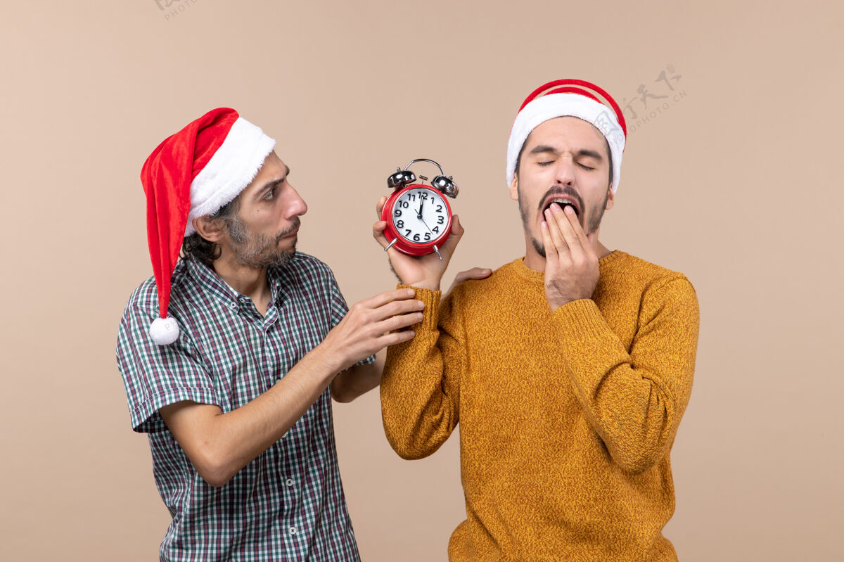 服装正面图两个男人 一个拿着闹钟 在米色孤立的背景上打哈欠面具男人成人