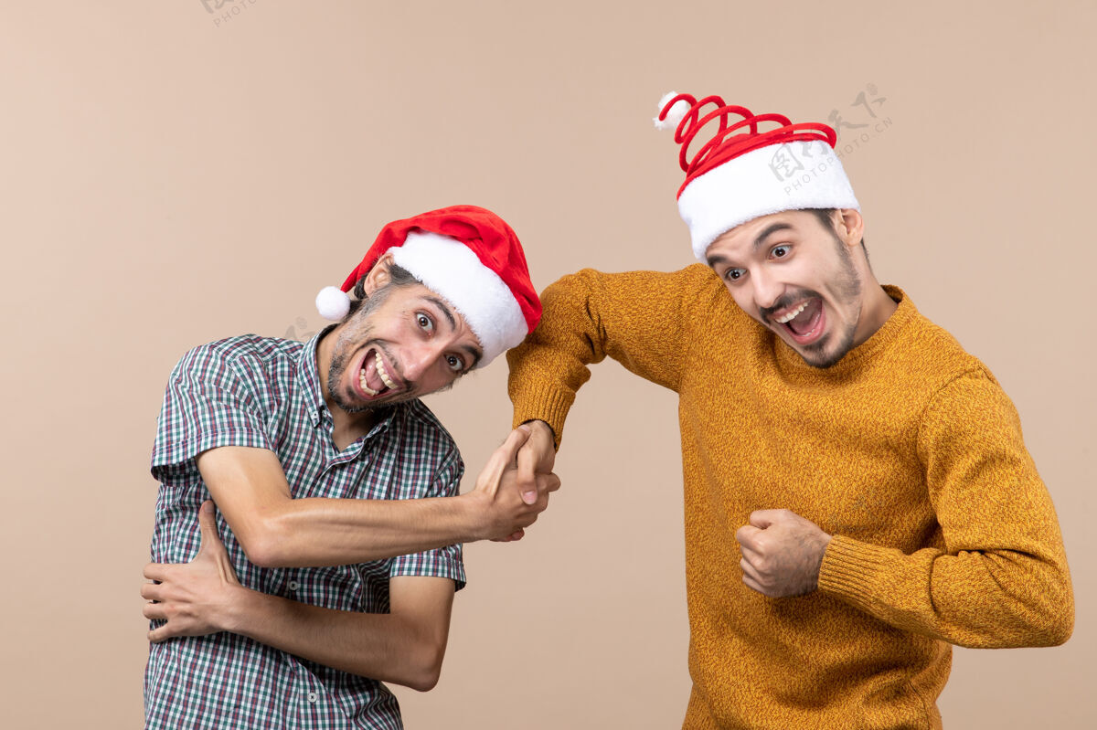 圣诞老人正面图两个戴着圣诞帽的快乐男人在米色孤立的背景上握手手米色颤抖