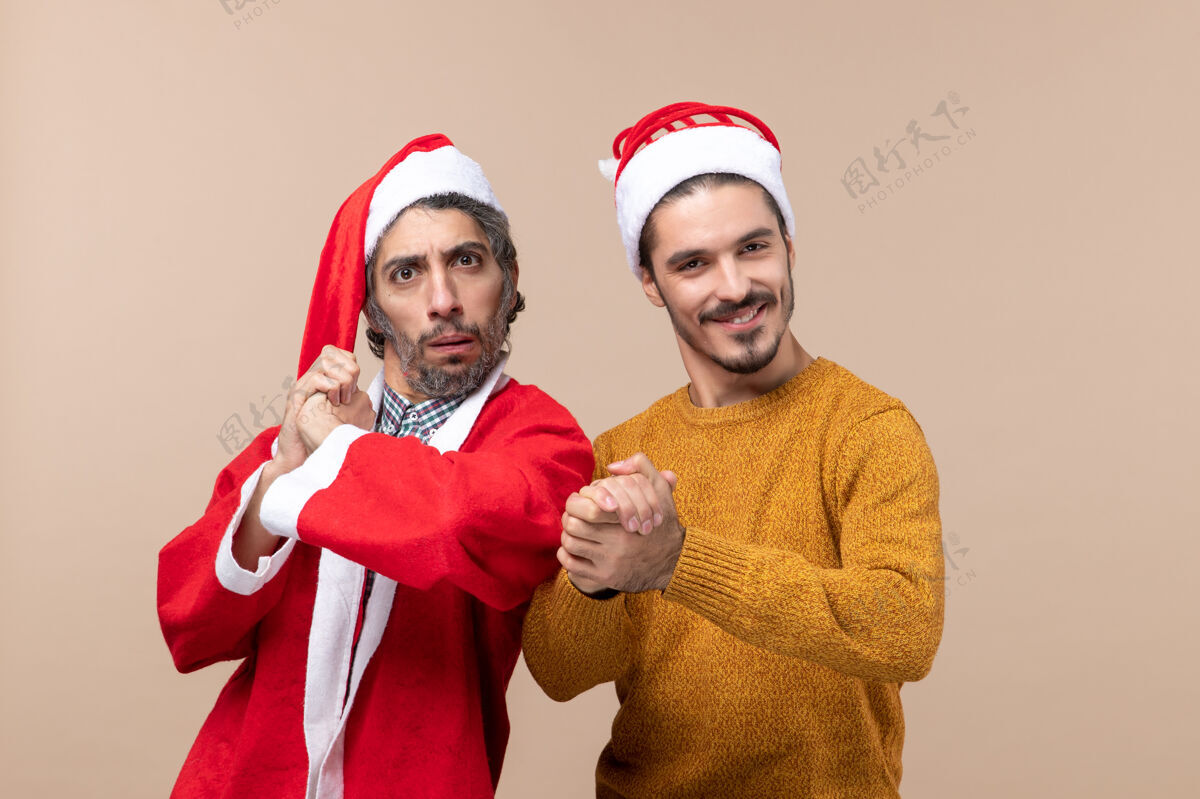 男人前视图两个圣诞节男子都紧握着双手米黄色孤立的背景男人微笑米色