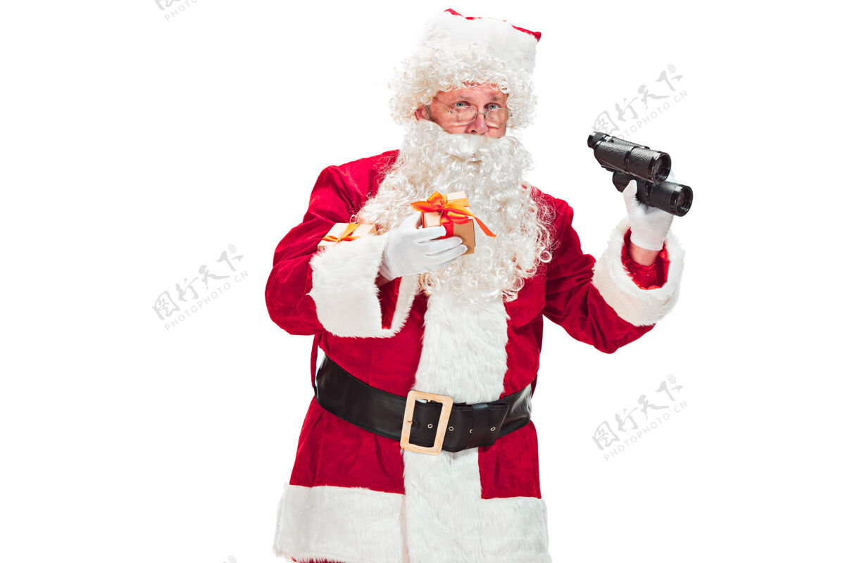 双筒望远镜一个穿着圣诞老人服装的人的肖像-有一个豪华的白胡子 圣诞老人的帽子和一个红色的服装-在一个白色的背景上用双筒望远镜孤立的全长圣诞节圣诞老人男性