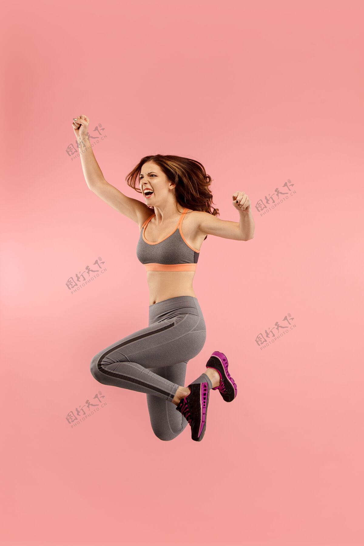 跳跃移动中的自由在橙色工作室背景下 美丽快乐的年轻女子跳跃和做手势的半空中镜头在运动中奔跑的女孩人类情感和面部表情的概念运动惊喜肖像
