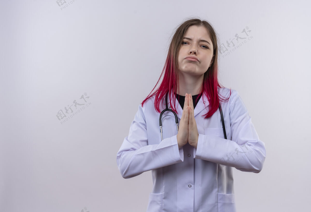 白色悲伤的年轻医生女孩穿着听诊器医用长袍 在孤立的白色背景上显示祈祷手势 并留有复印空间女孩祈祷空间