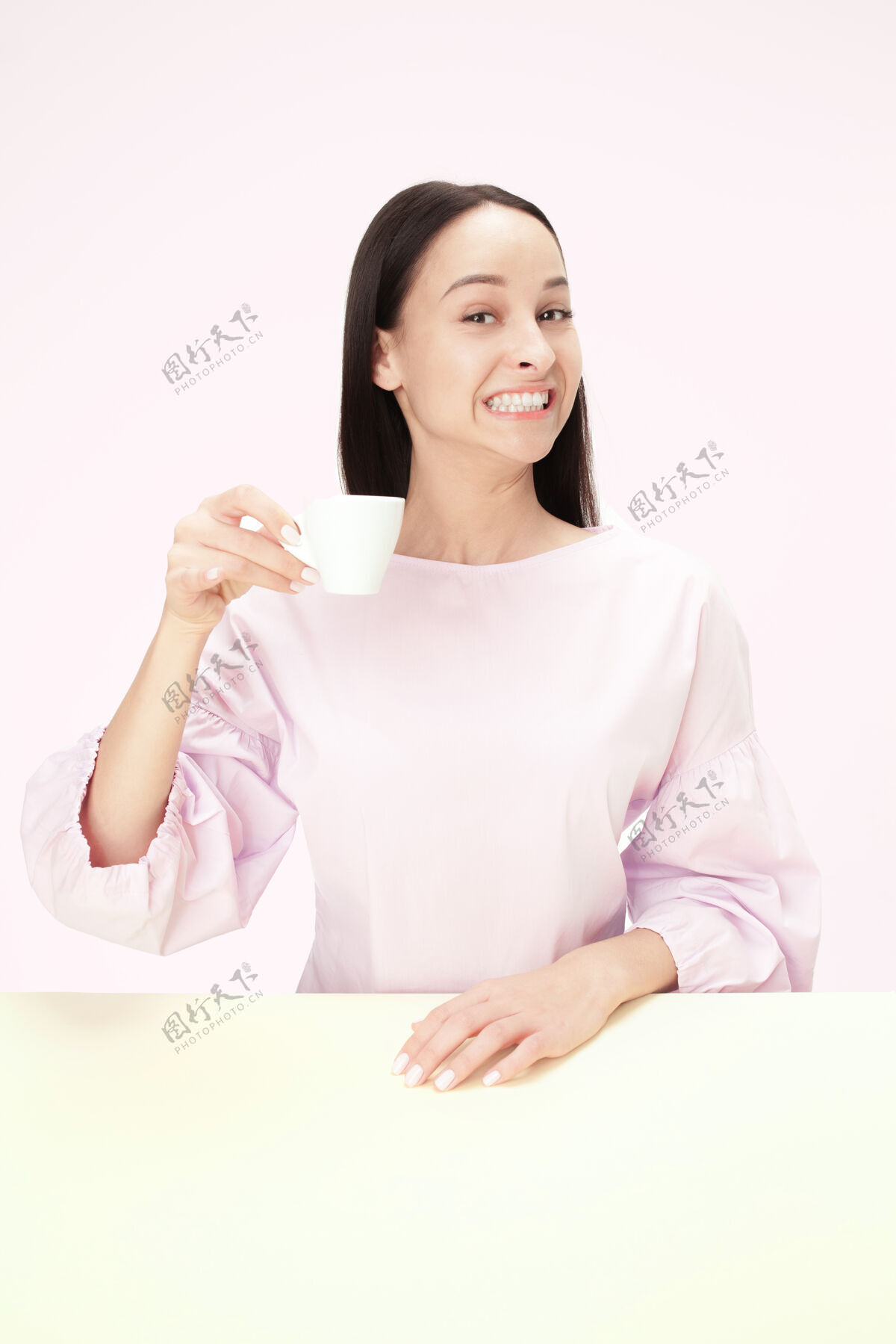 简约美丽的微笑的女人坐在粉红色的工作室里 手里拿着一杯咖啡 看起来很开心咖啡茶沉思