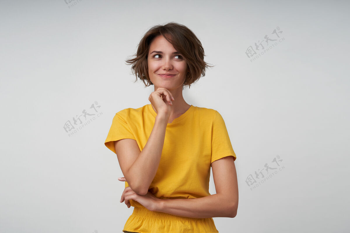 摆姿势可爱的年轻黑发女性 随意的发型 下巴靠在抬起的手上 正眼望向一边 摆出黄色t恤的姿势积极自然色漂亮