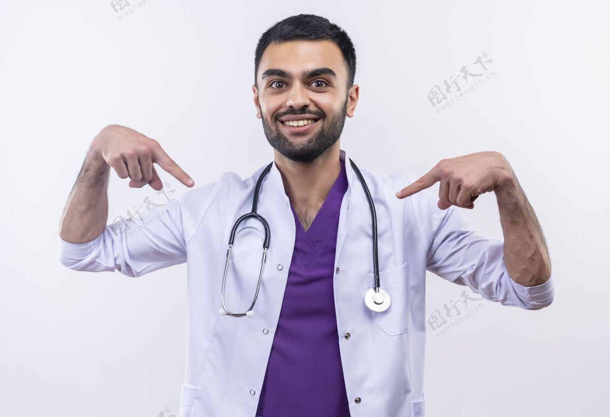 听诊器身着听诊器医用长袍的年轻男医生微笑着指着孤立的白色背景上的自己医疗男性分