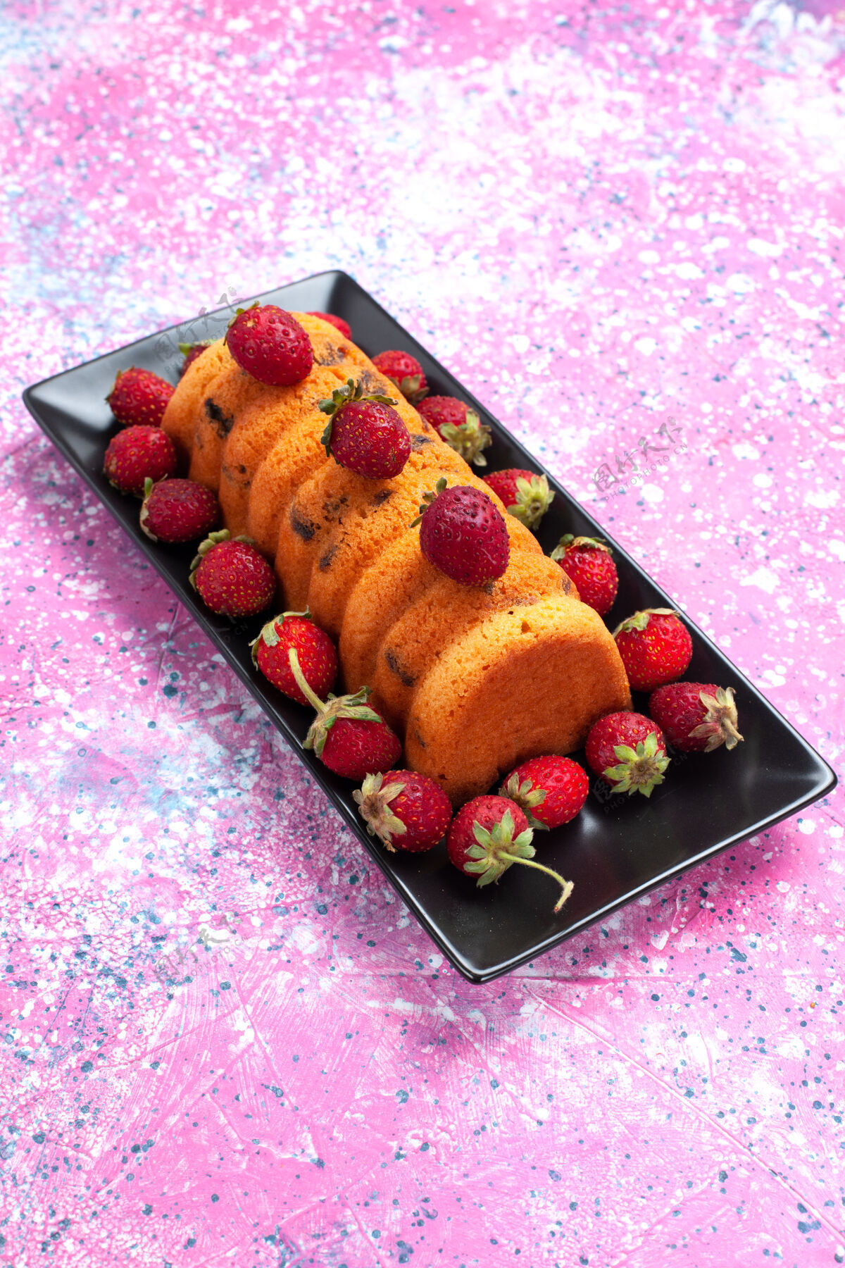 饼干正面是美味的烤蛋糕 放在黑色的蛋糕锅里 粉红色的桌子上放着新鲜的红色草莓黑色水果甜点