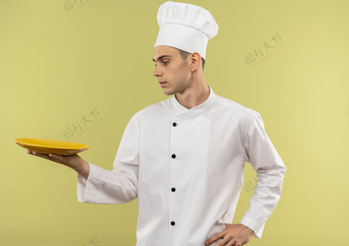 厨师站在侧视图年轻的男厨师穿着厨师制服看他的手把他的手放在臀部与复制空间板手厨师男
