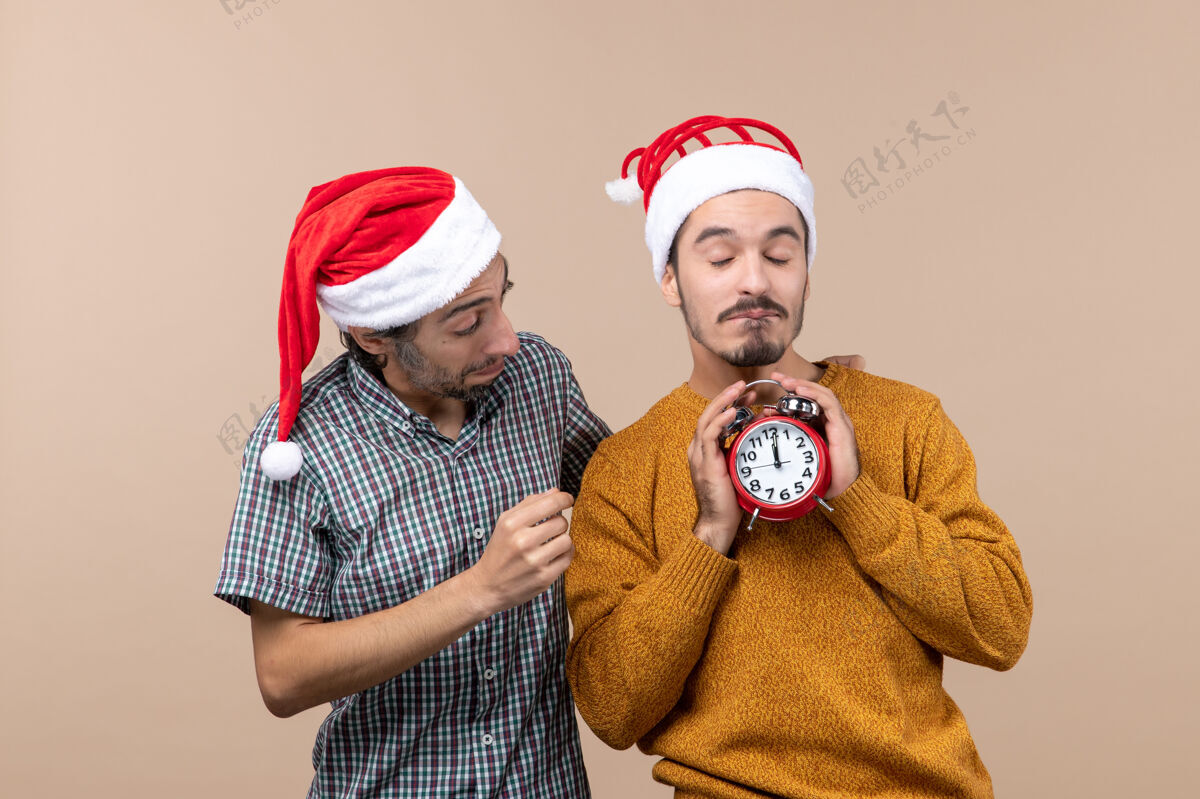 情侣正面图两个圣诞老人一个拿着闹钟双手放在米色的隔离背景上男性男人圣诞节