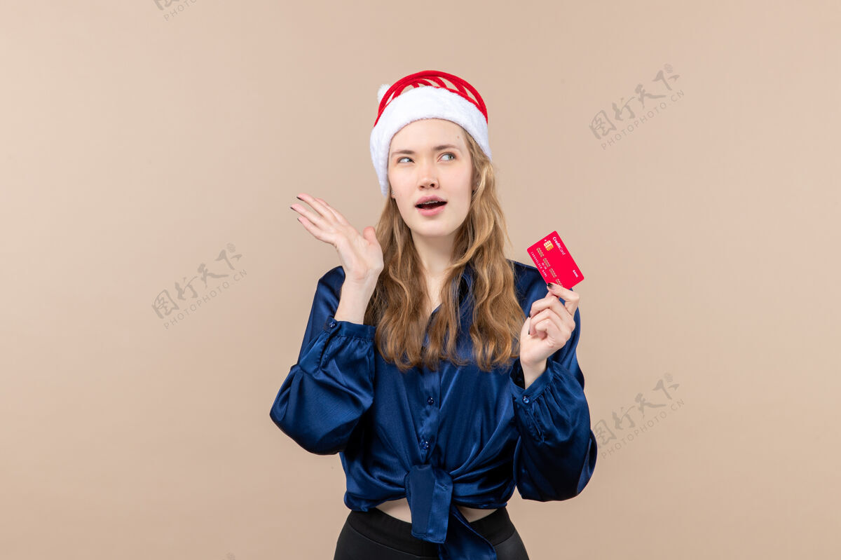 年轻人正面图年轻女子手持红色银行卡上一张粉色背景的钞票照片假日新年圣诞感慨帽子肖像微笑